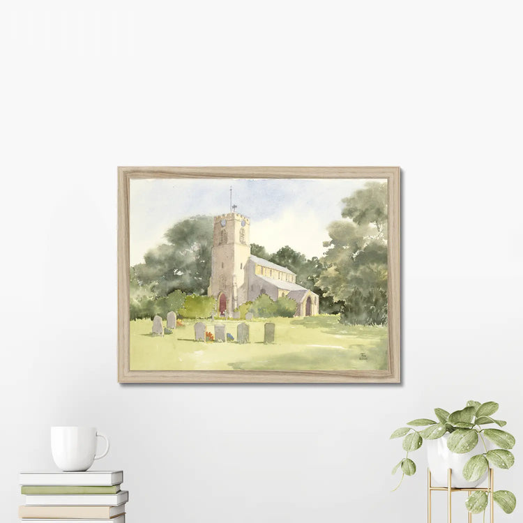 Framed print of a church hanging on a white wall above books and a plant