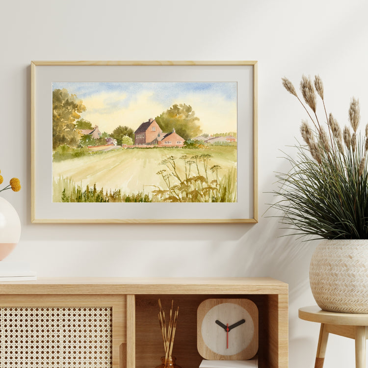 Framed and mounted print of a farm hanging on a wall above a modern sideboard