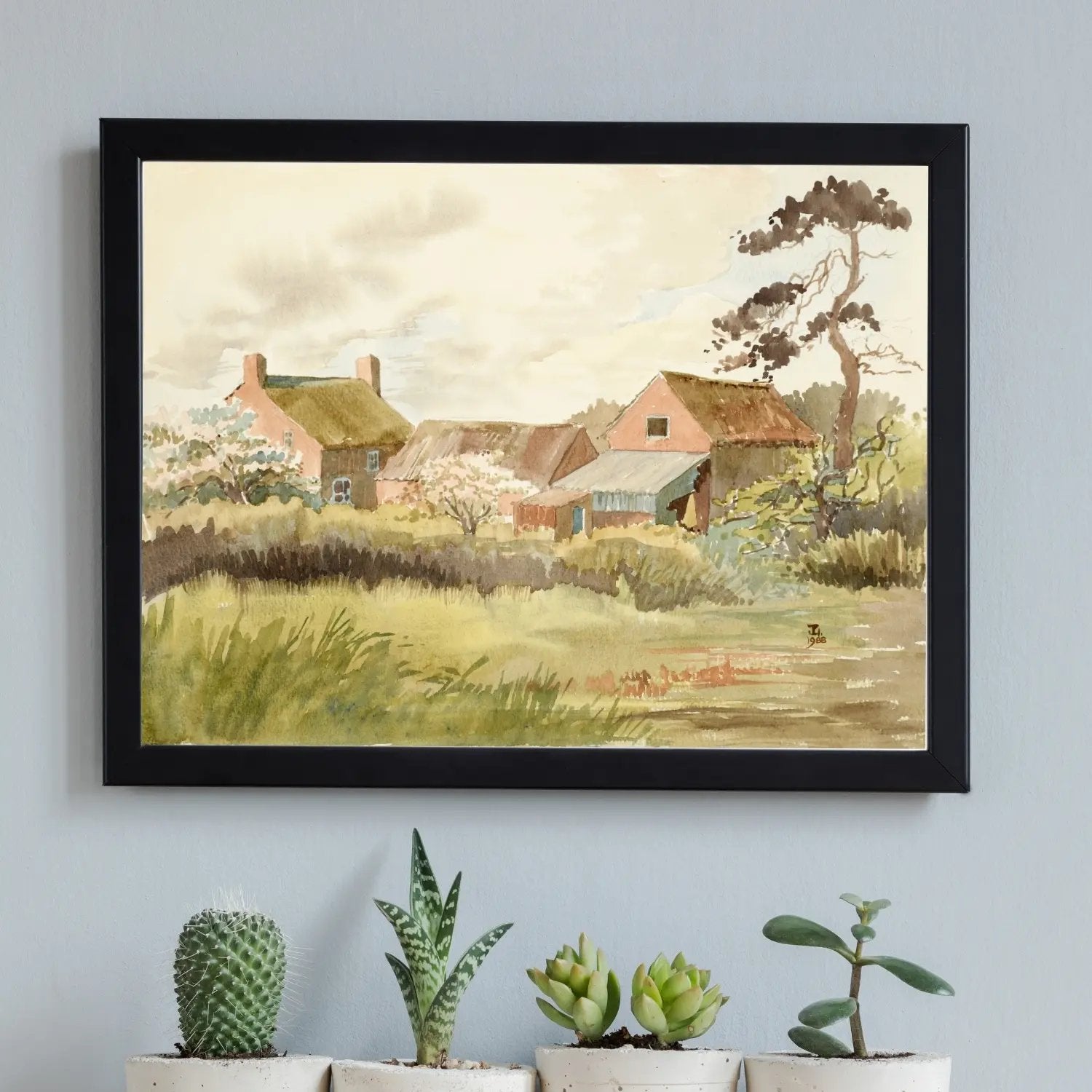 Black framed print of a farm hanging above four small cactii