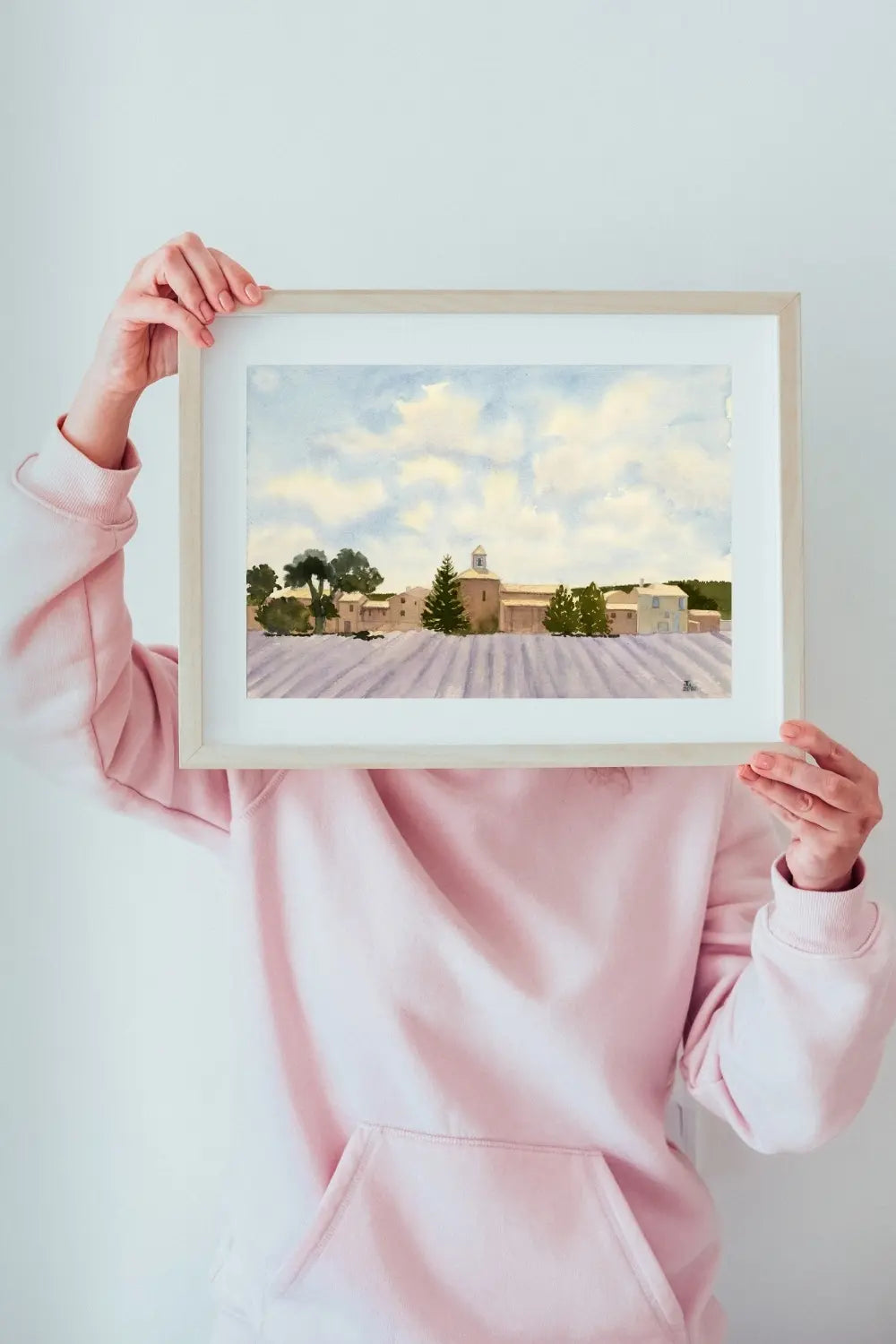 Woman in a pink hoodie holding up a framed and mounted print